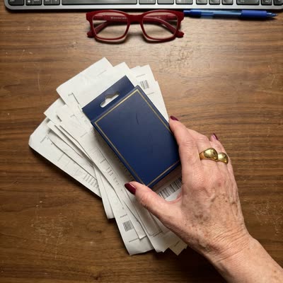 Desk flat-lay — manicured hand pushing aside a stack of Kerasal and Kerassentials receipts to hold up a NailScience 3-pack bundle